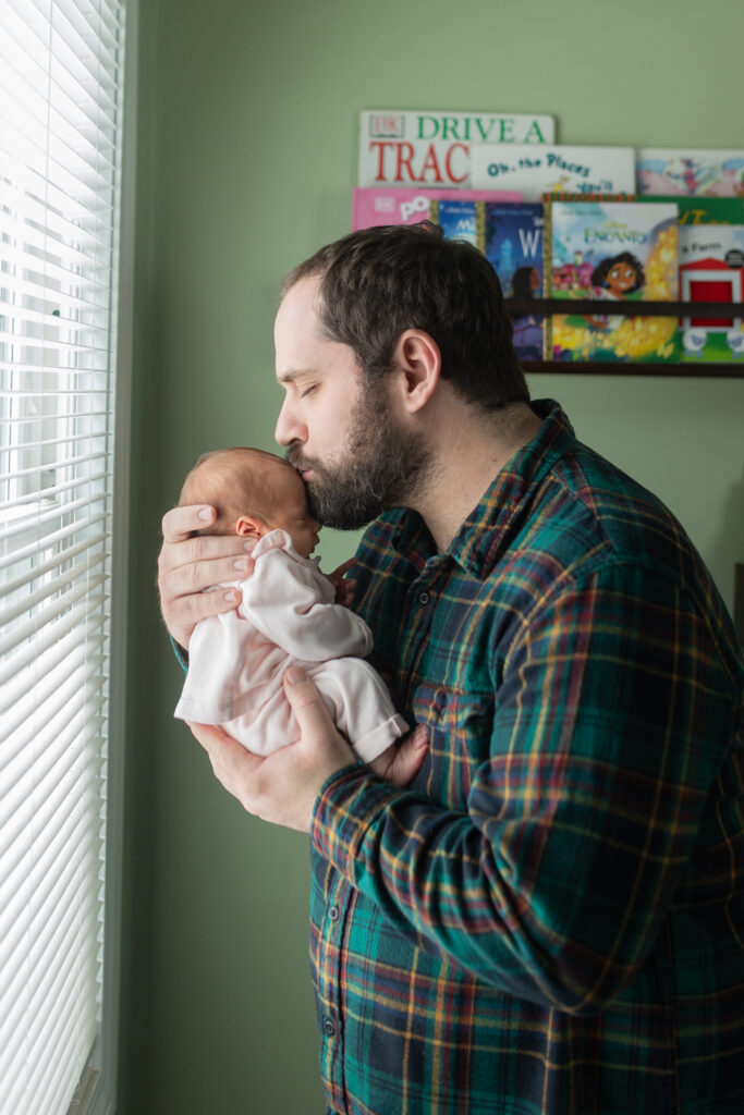 Dad kissing baby on forehead while facing window